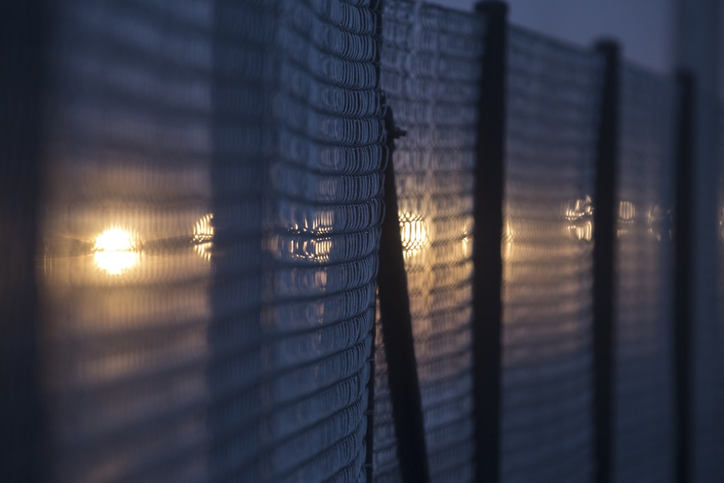 image of a wire fence at night, backlit by orange lights
